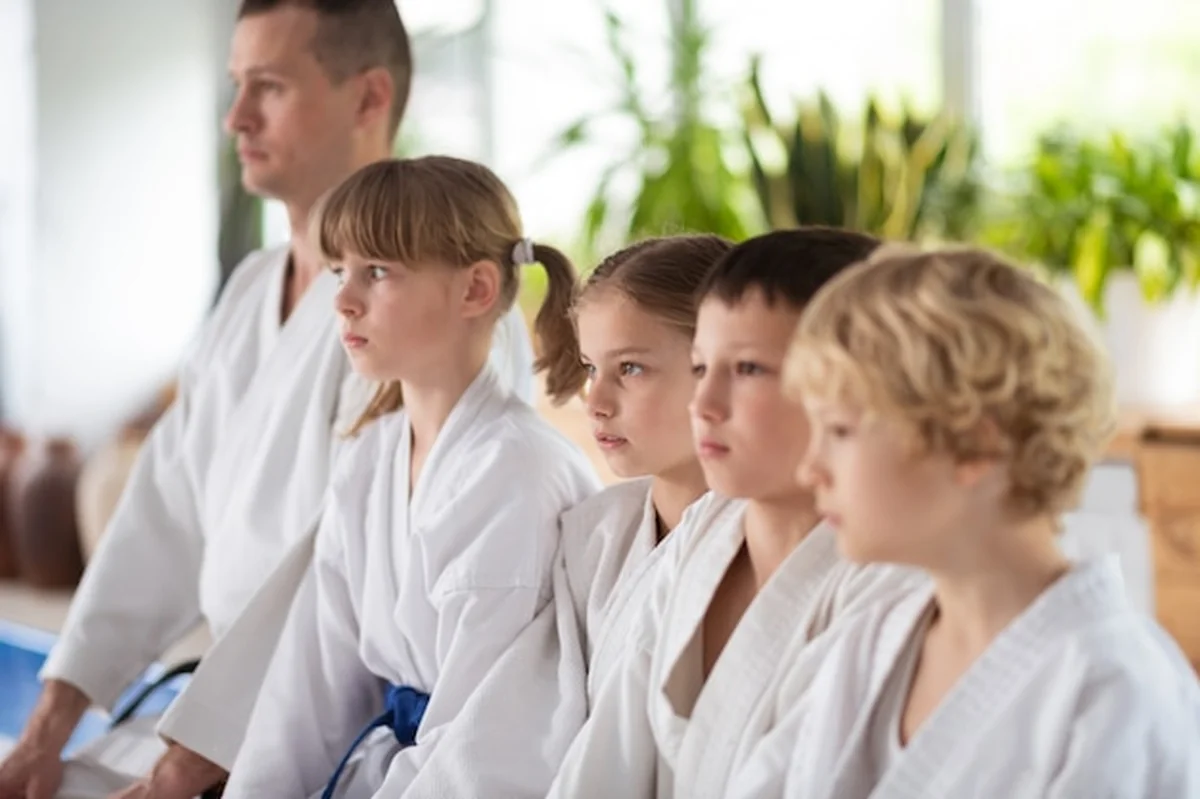 Trener z dziećmi w białych kimonach siedzący na podłodze