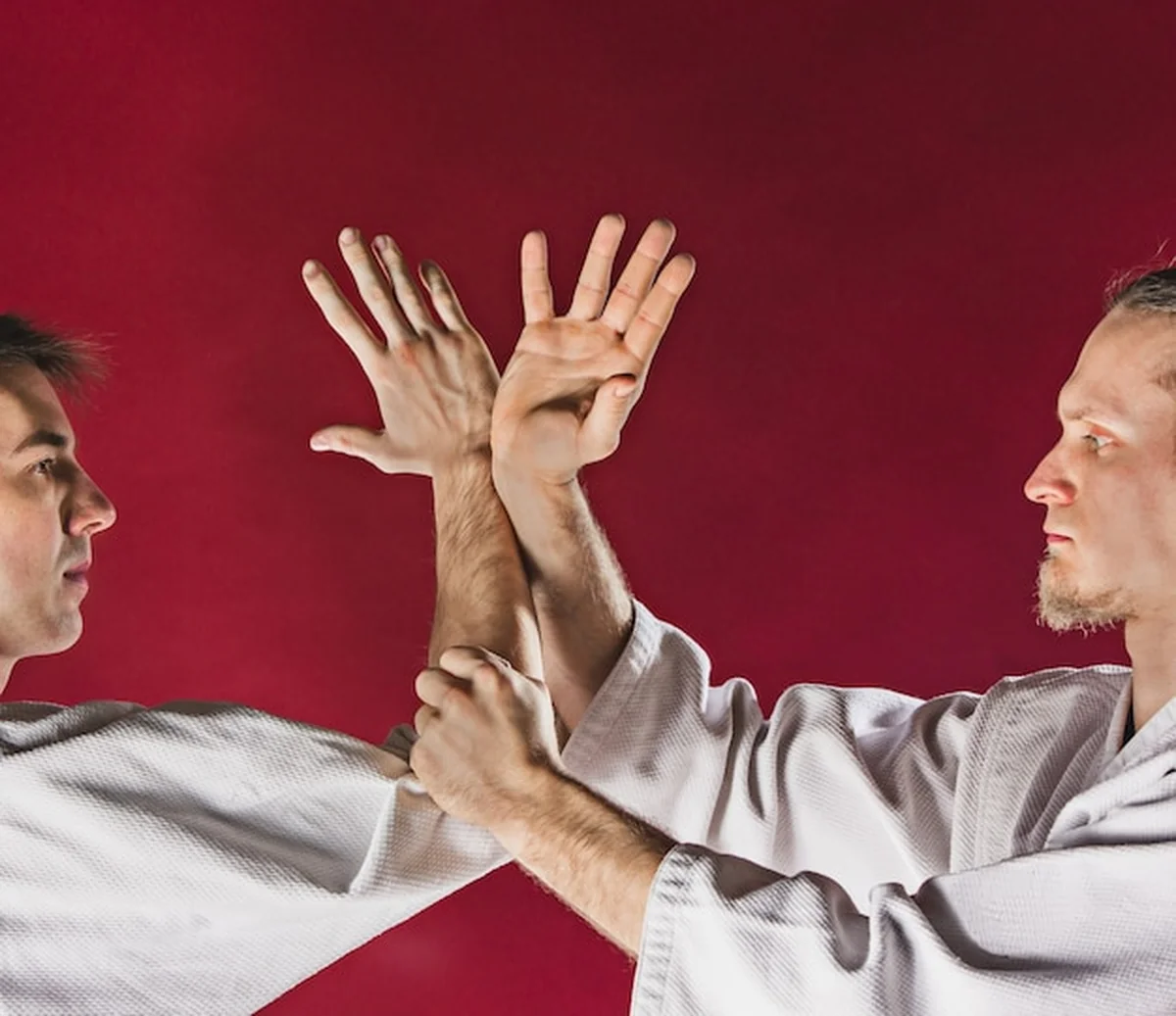 Dwóch mężczyzn w białych kimonach na czerwonym tle trenujących aikido w szkole sztuk walki
